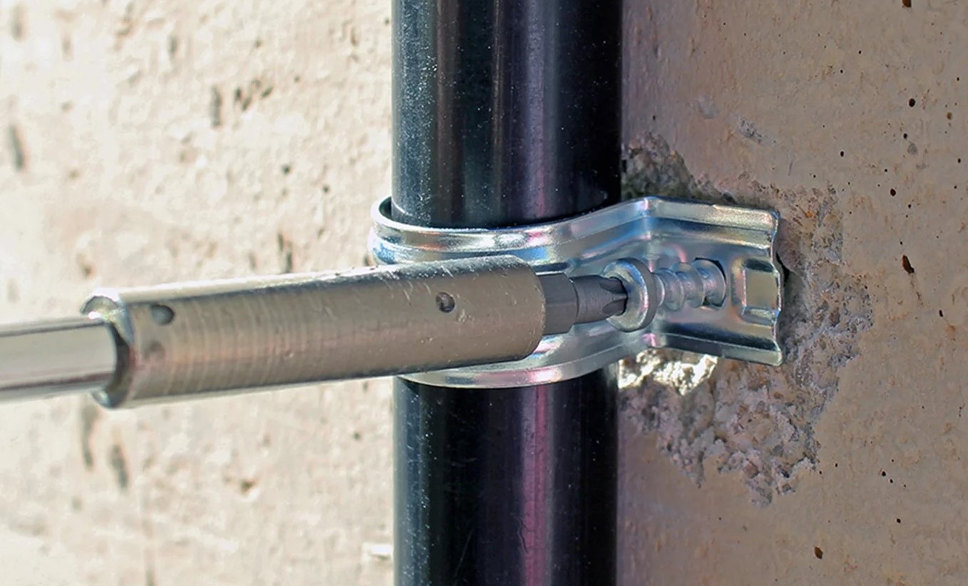 Montagebild der Betonschraube BTS4 PT, ein Metallclip umschließt ein schwarzes Rohr und wird an einer Betonwand mit der neuen Betonschraube festgeschraubt